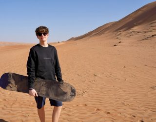 Tiener met sandboard in woestijn van Oman
