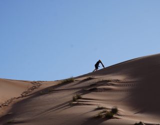 Tiener klimt met sandboard op zandduinen van Oman