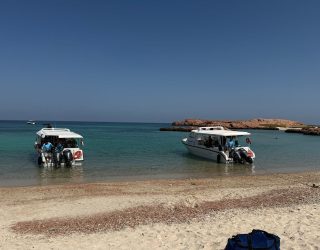 Boten aan strand met helderblauw water in Oman
